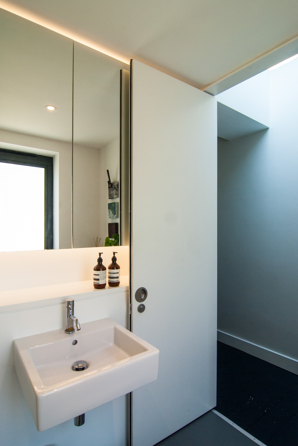 Minimal palette bathroom offers plenty of light to reflect off the mirrors facing the window.