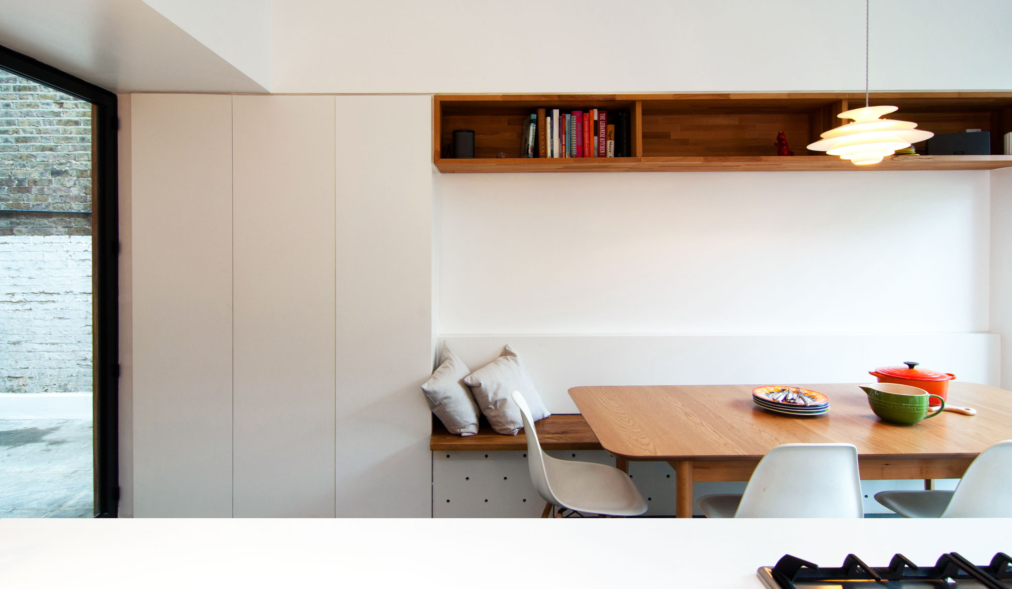 New kitchen extension highlighting key details such as the timber bookshelf and bench within the white contemporary storage cabinets.