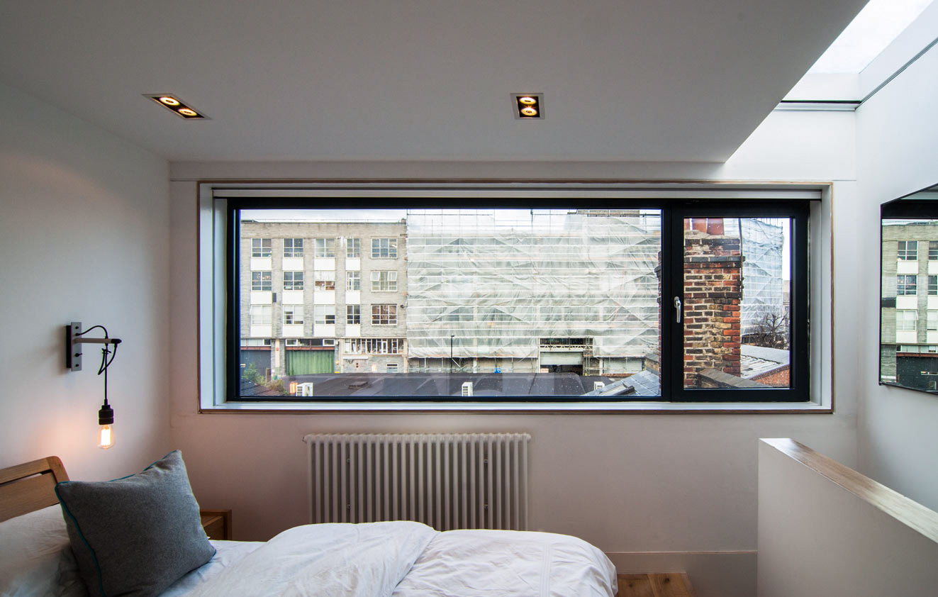 Large horizontal bedroom window and roof light with minimal artificial lighting in the converted loft bedroom.