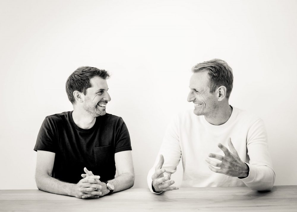 George Bradley and Ewald Van Der Straeten, founders of Bradley Van Der Straeten Architects, sitting together, smiling confidently, representing the studio’s expertise in period and contemporary London homes.