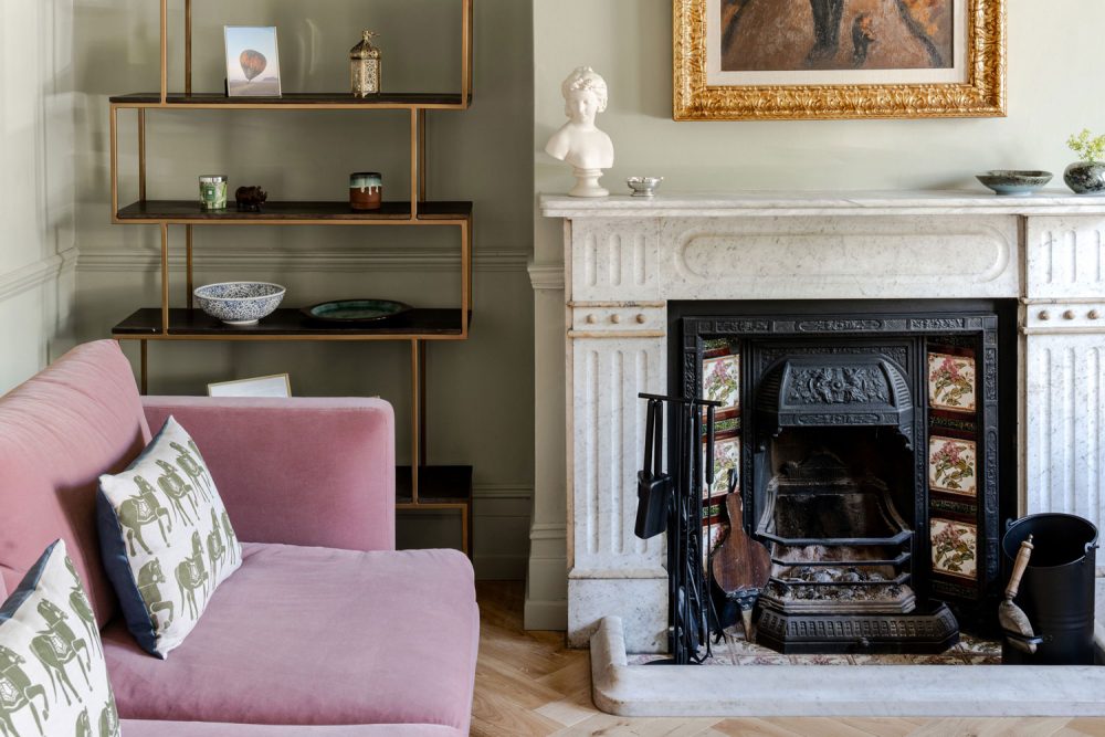 Green-painted living room in a London period home, featuring an ornate fireplace and gilded picture frame, blending historic character with modern comfort.