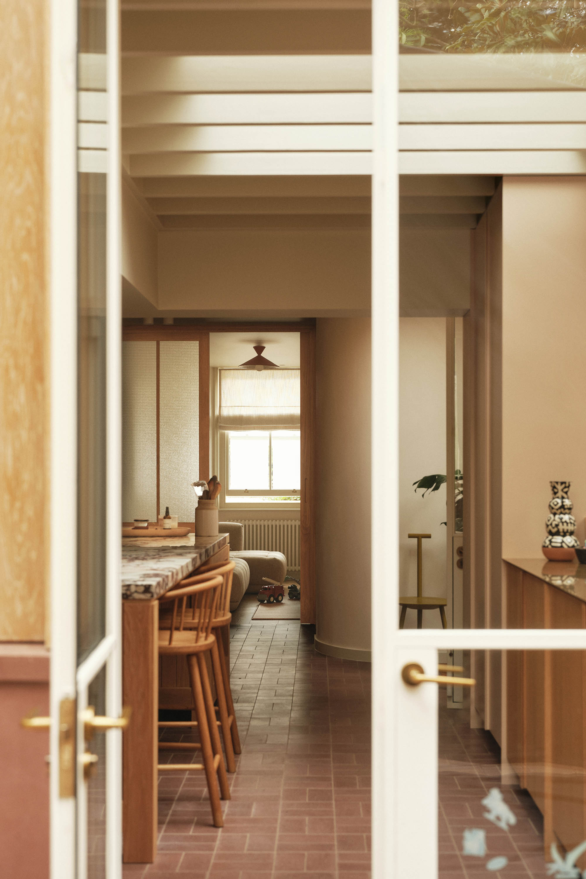 Lauriston kitchen with glazed Crittall doors, central island with marble, oak bespoke joinery, exposed ceiling joists, and red paved tile floor