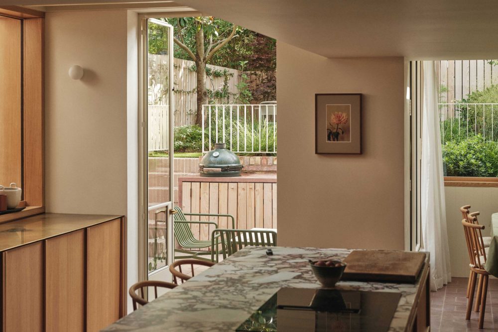 Lauriston kitchen with central island, oak bespoke joinery, Cr ittal door opening to the garden, wall-mounted globe light, and Clayworks finishes.