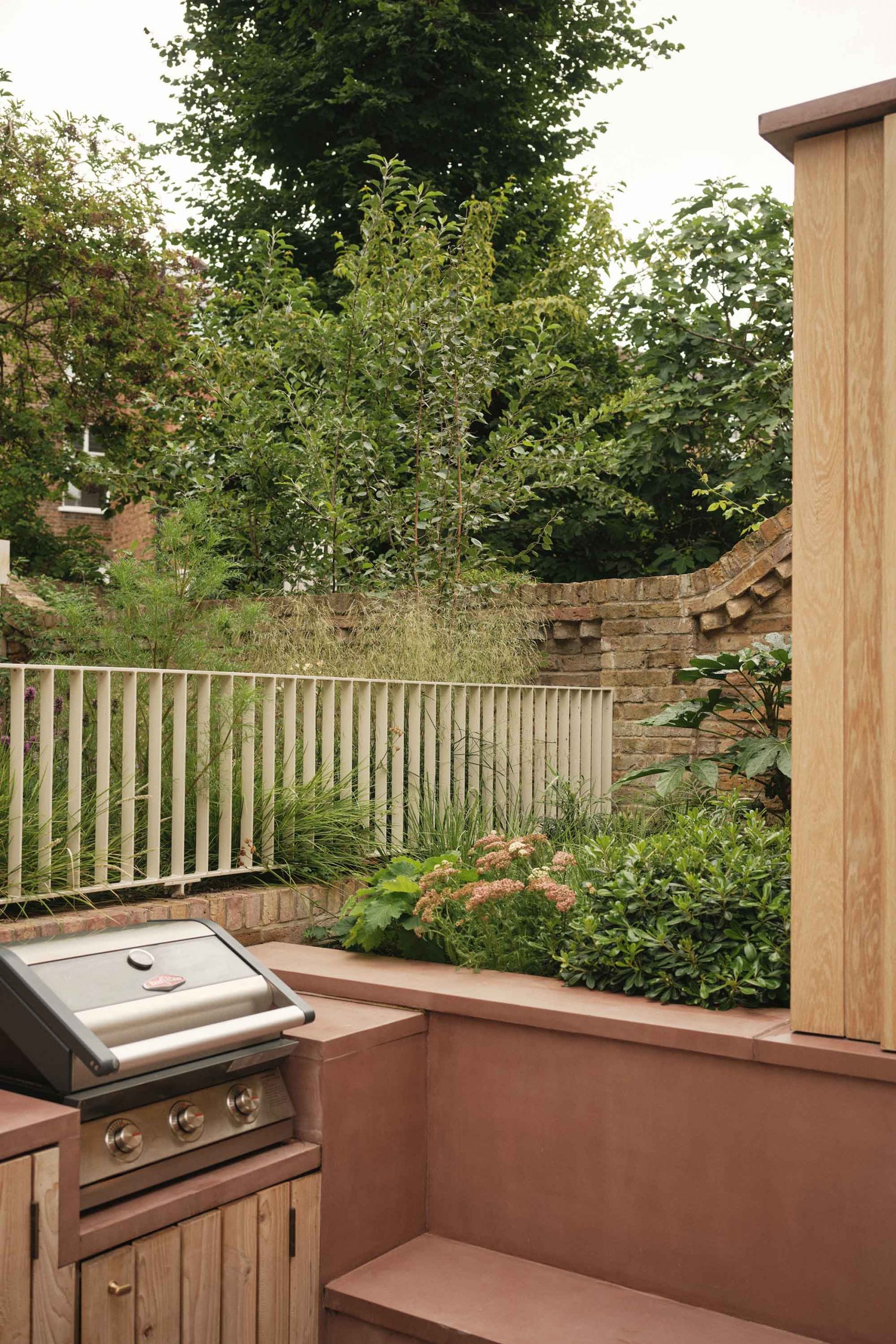 Lauriston outdoor dining area with pink concrete bench, bi-fold window, oak panelling, raised planter, and garden view.