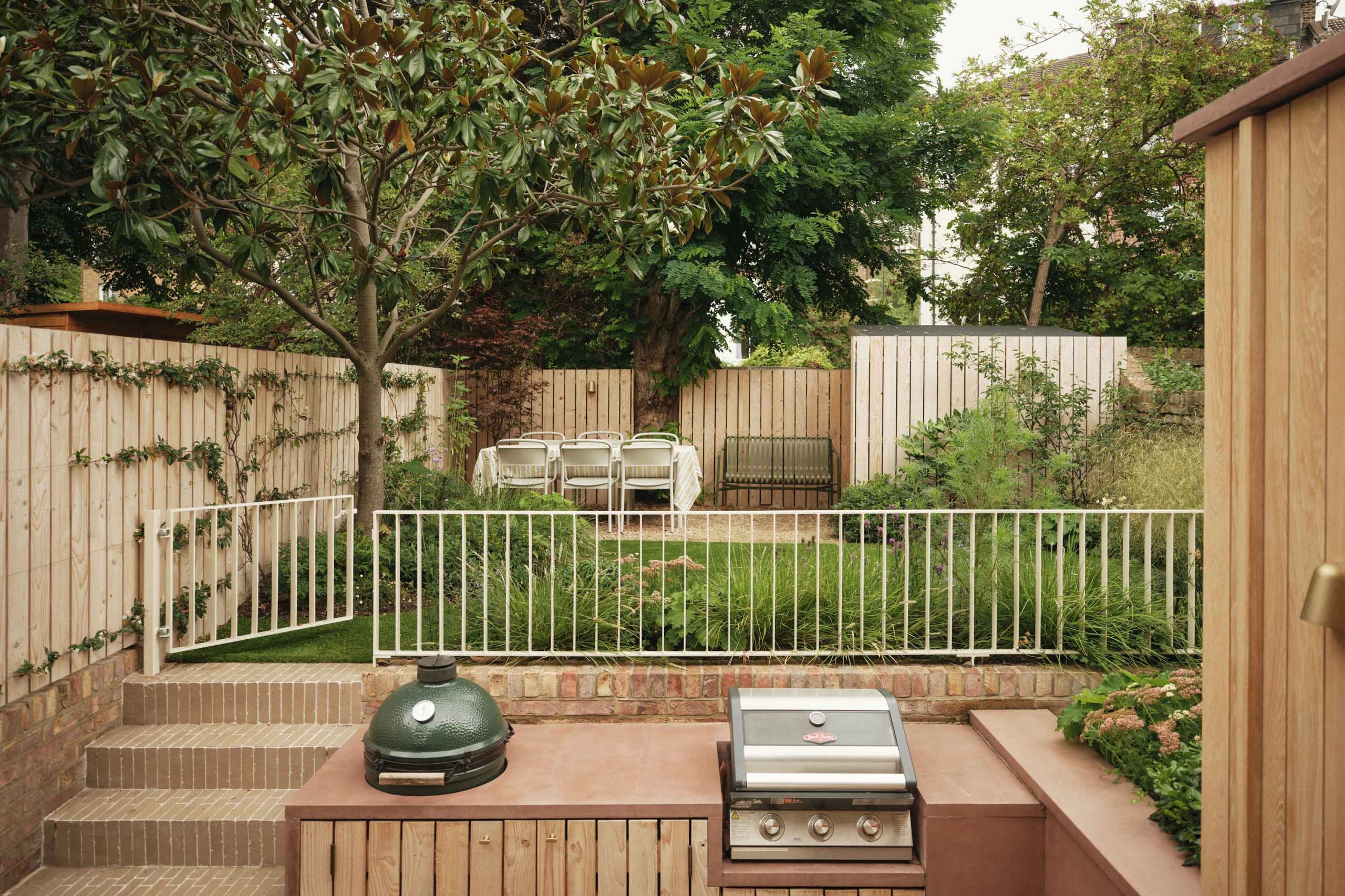 Lauriston raised garden patio featuring outdoor kitchen with built-in Green Egg BBQ, pink concrete worktop, and metal railing balustrade.