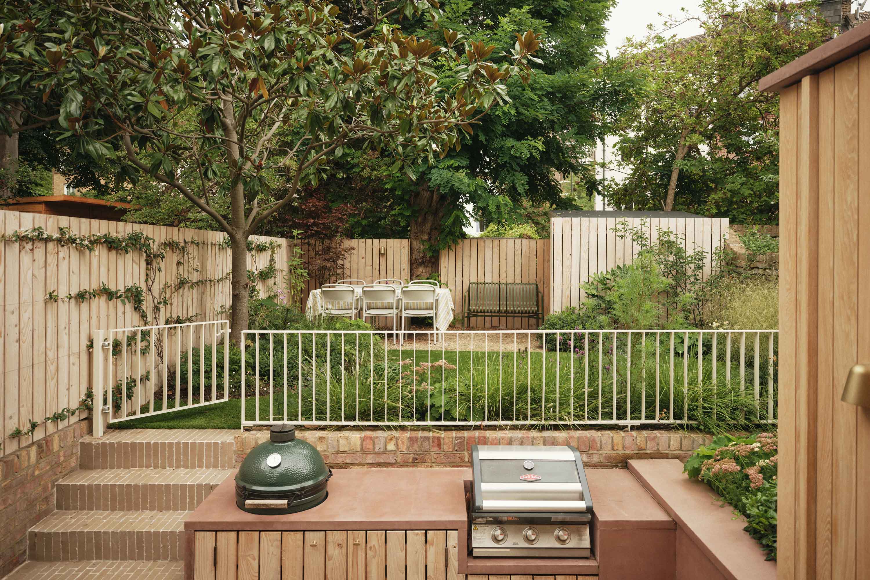 Lauriston raised garden patio featuring outdoor kitchen with built-in Green Egg BBQ, pink concrete worktop, and metal railing balustrade.