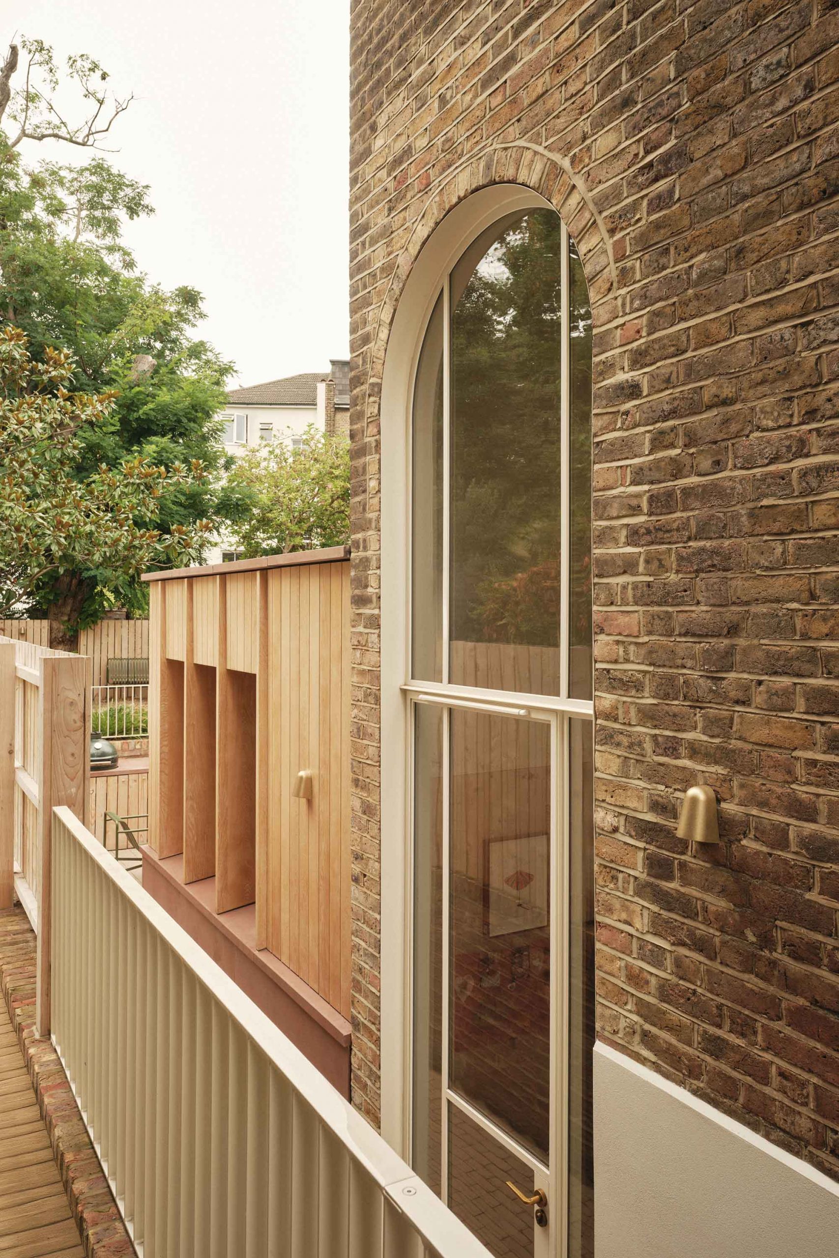 Lauriston side passage view showing double-height Crittall door, oak panelling, timber fins, and glimpses of the stepped garden beyond.