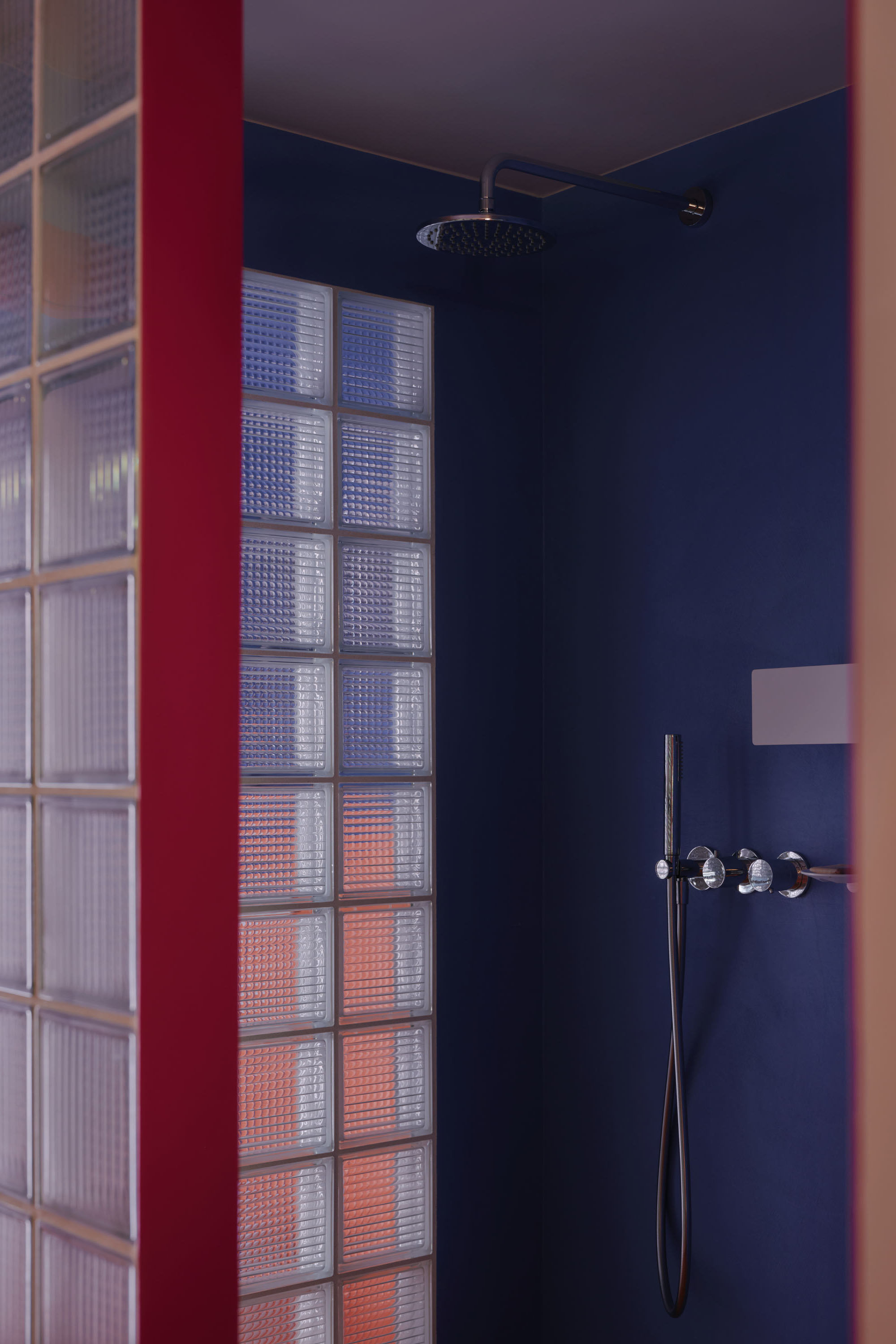 Modern bathroom extension with dark navy walls, glass brick partition, and rainfall shower fixtures.