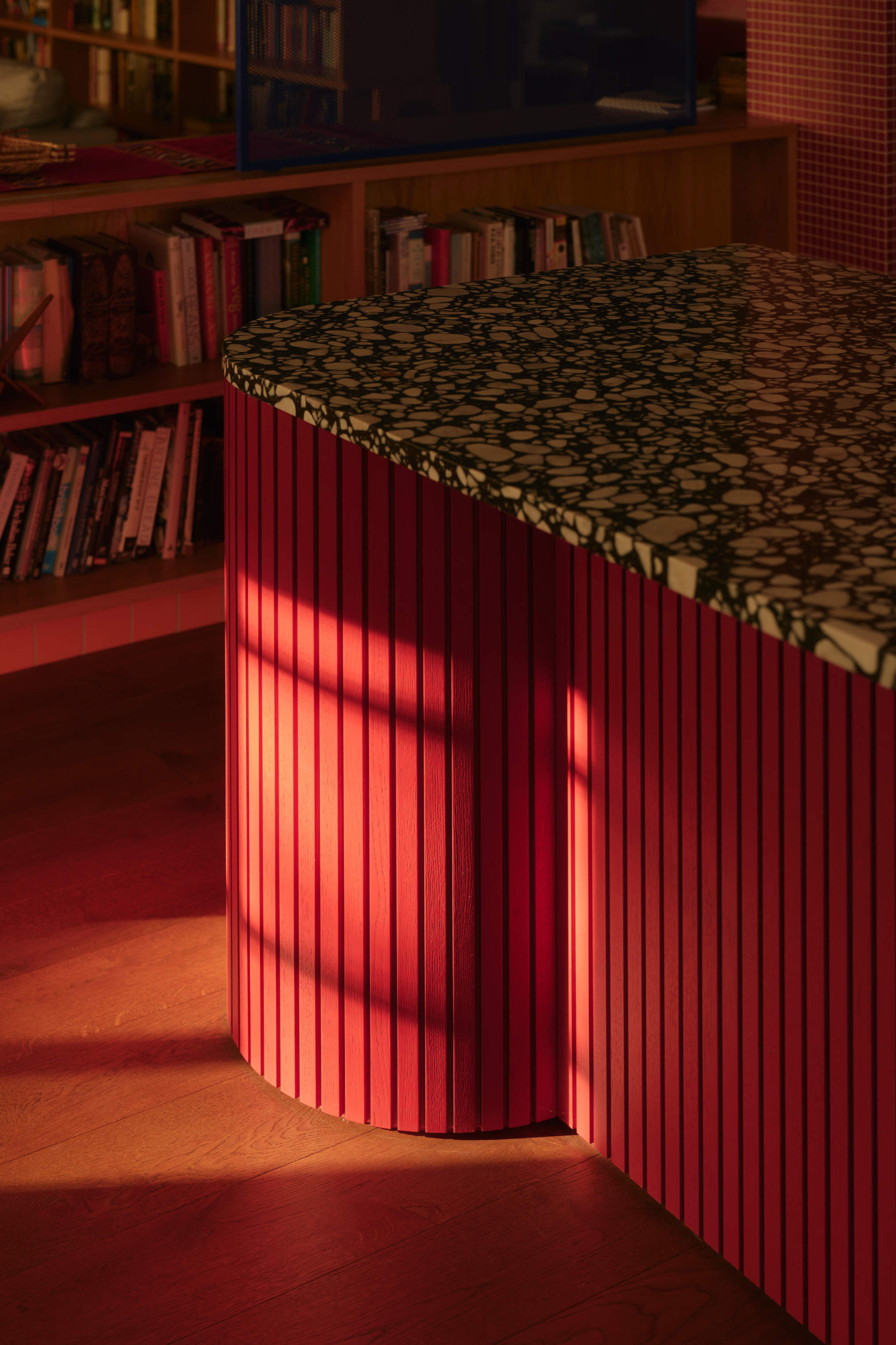 Built-in storage bench with red timber slats and patterned countertop creates functional kitchen extension seating.
