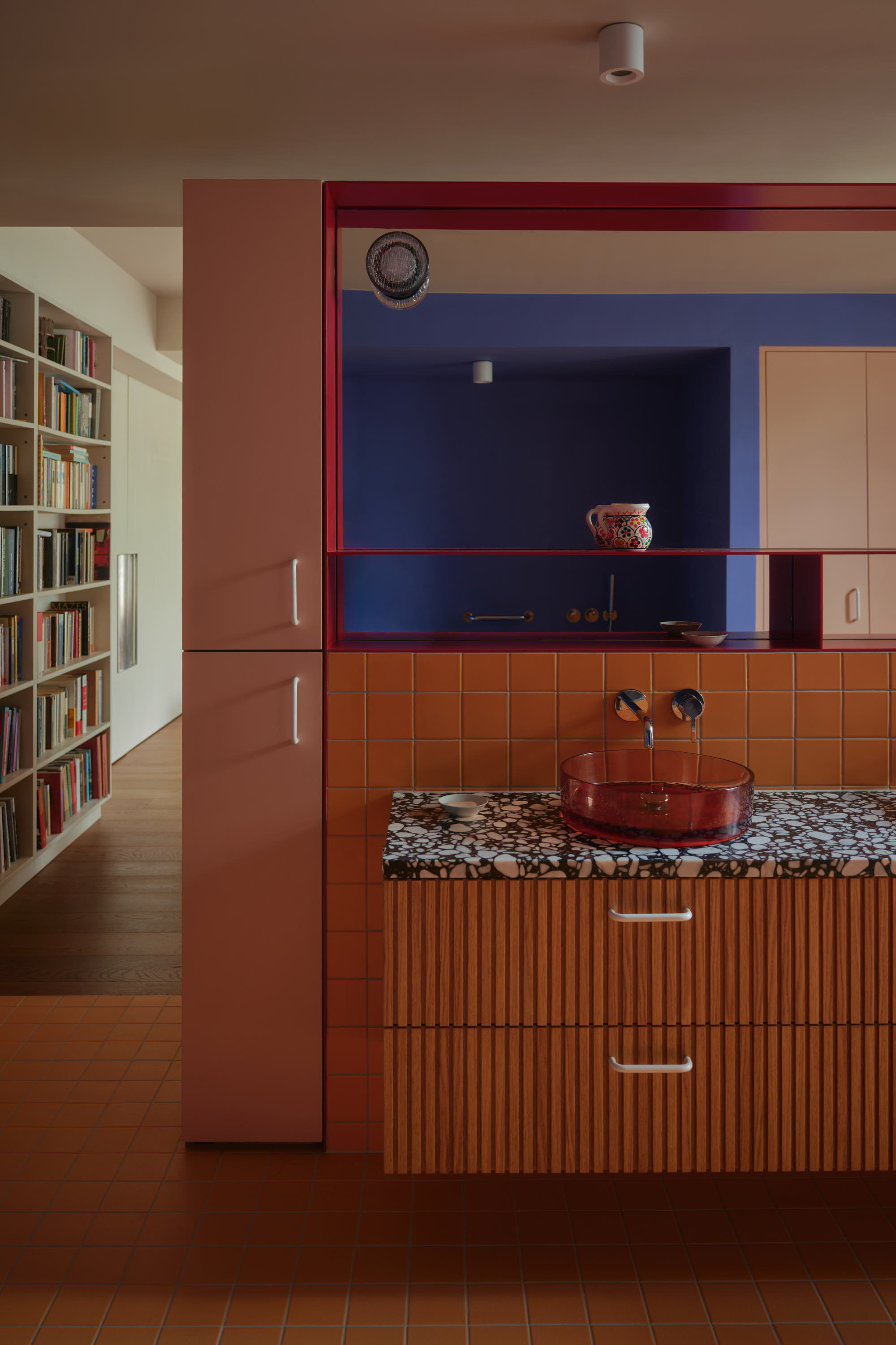 Modern kitchen extension with terracotta tiles, red cabinetry, and open plan living connecting to library space.