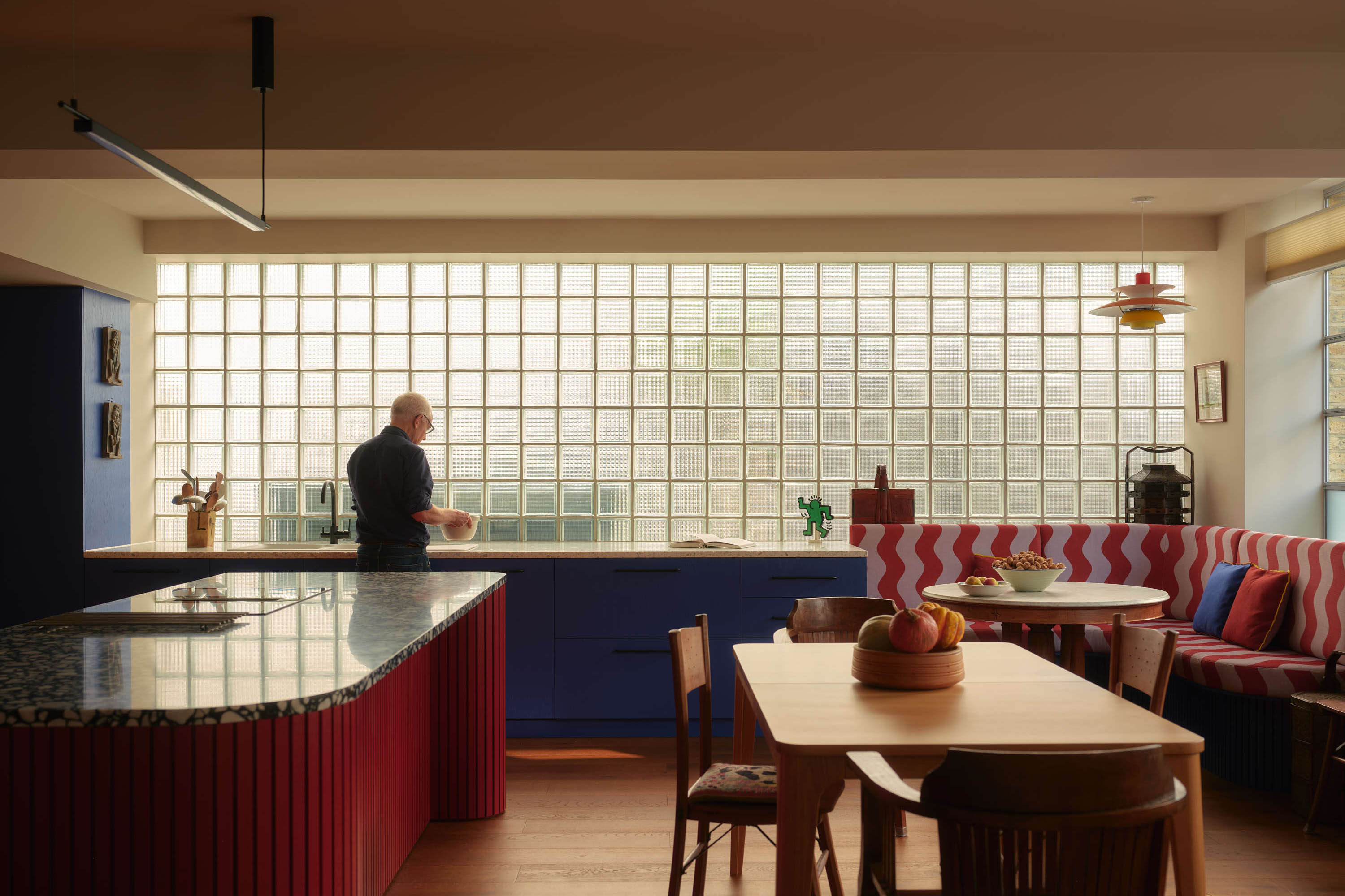 Open plan kitchen extension with glass brick wall, red cabinetry and integrated dining seating.