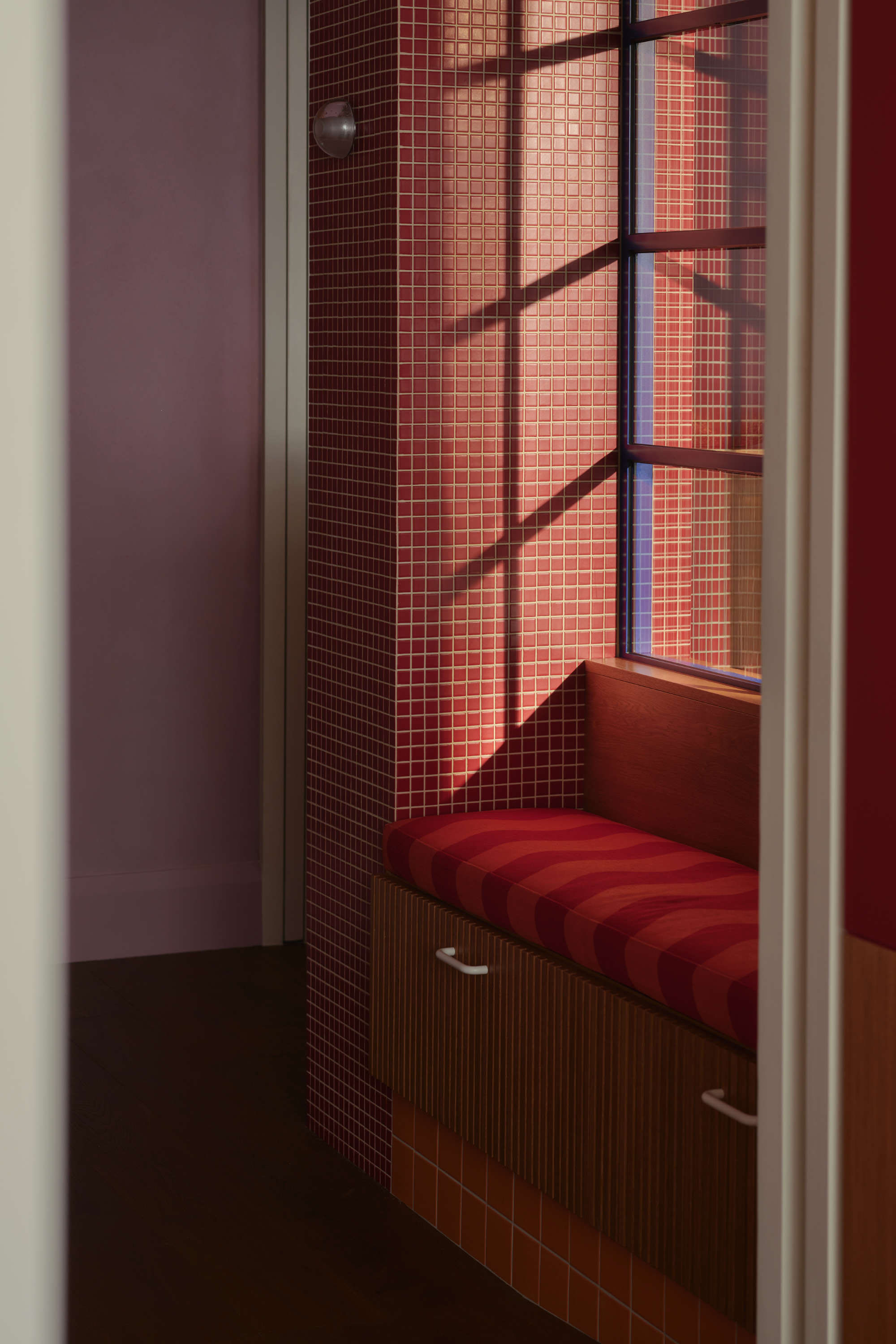 Brick tile window seat with red cushion and black steel frame. Modern house extension.