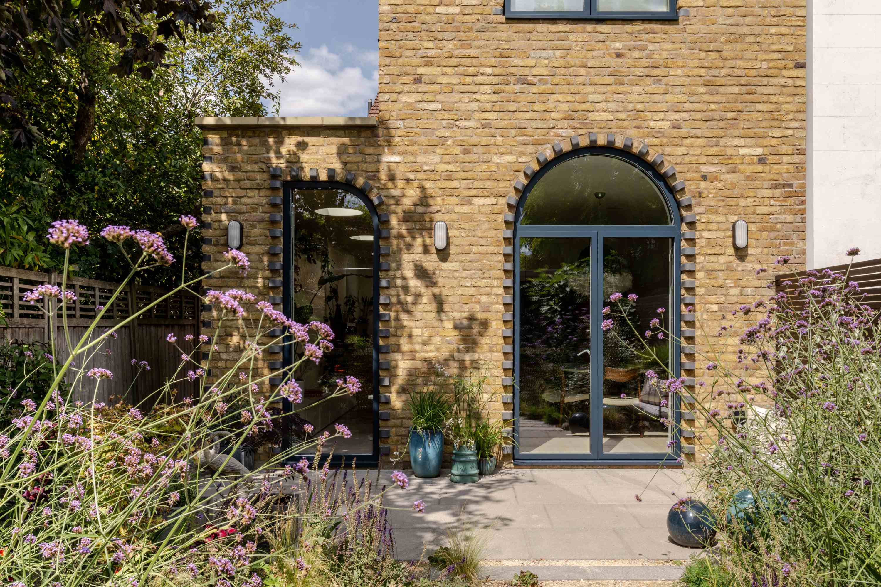 Brick rear extension with arched windows and contemporary glass doors opening to garden landscape.