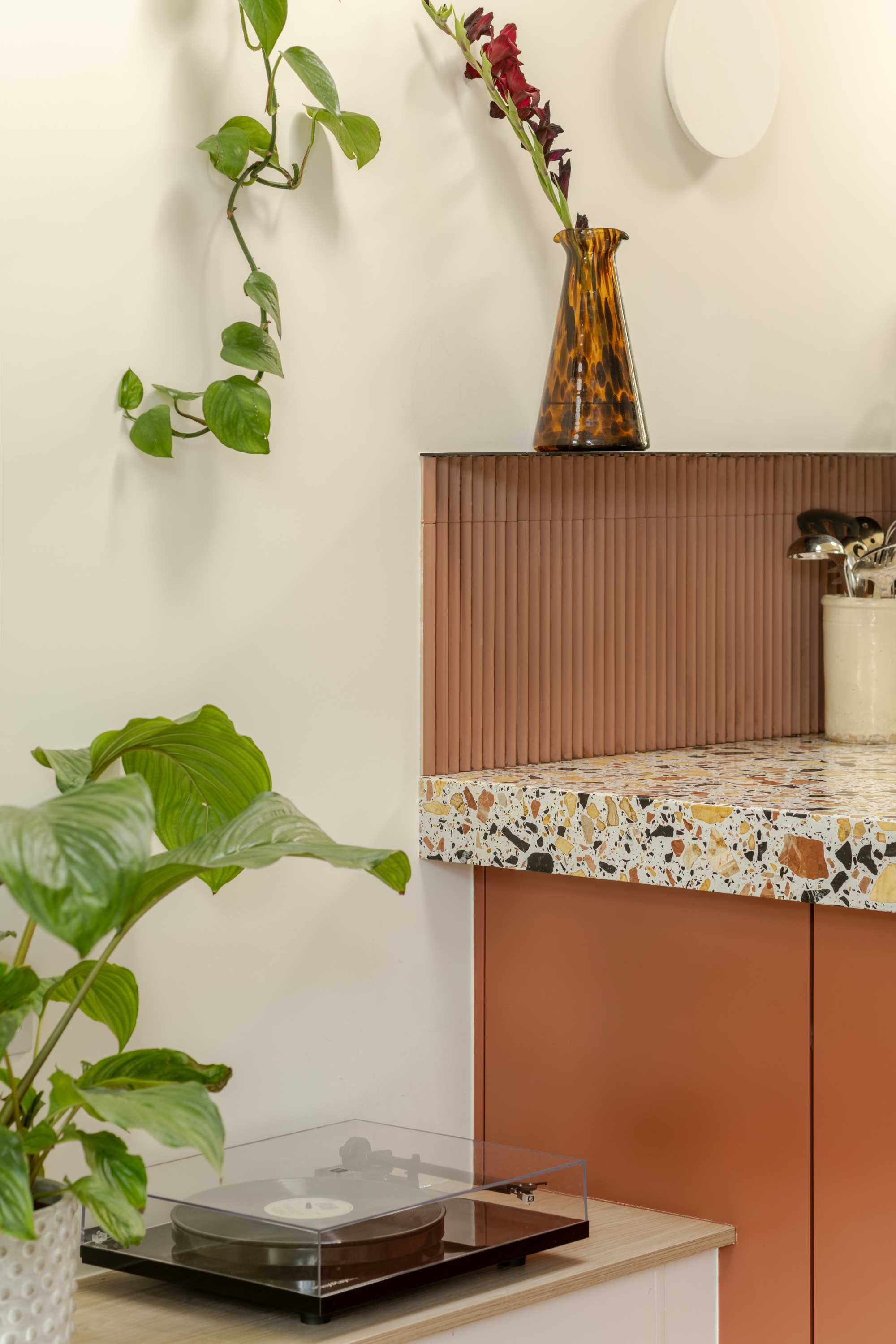 Terracotta corrugated cabinetry with terrazzo shelf top creates warm open plan living storage detail.