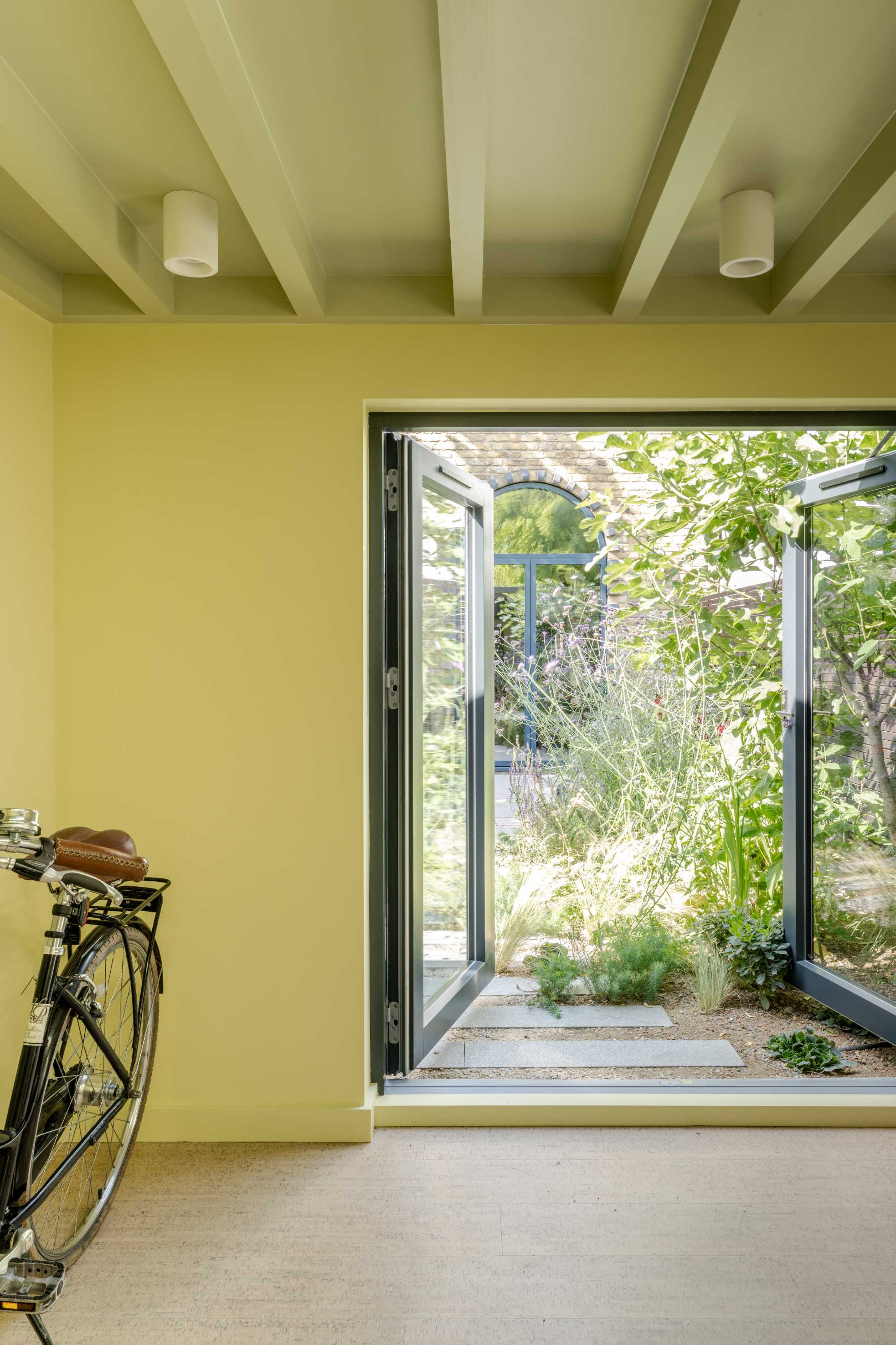 Bright garden room extension with yellow render walls, exposed beam ceiling, and wide glass doors opening to landscaped garden.
