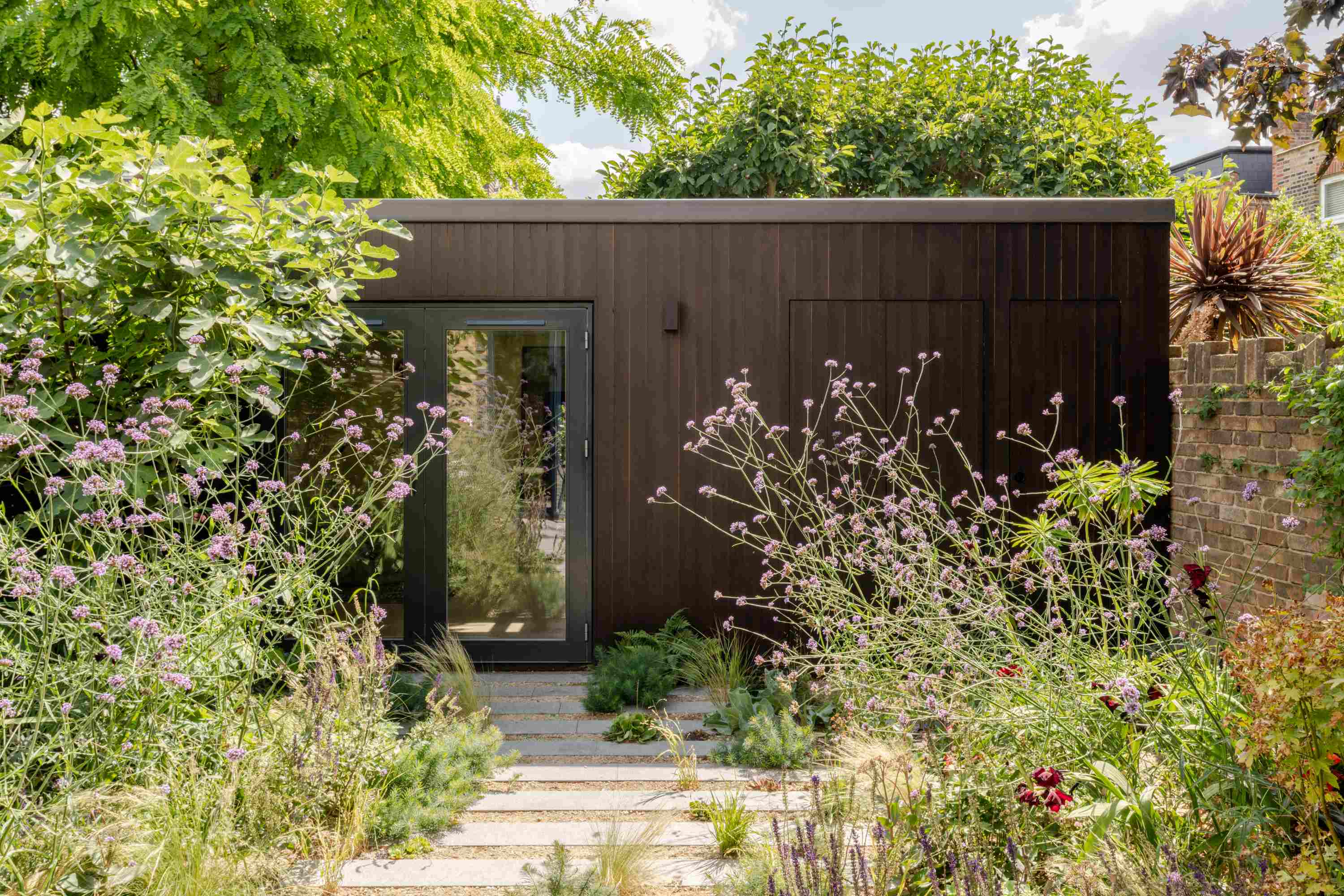 Contemporary garden studio with charred timber cladding and minimalist glazed entrance surrounded by flowering perennials.
