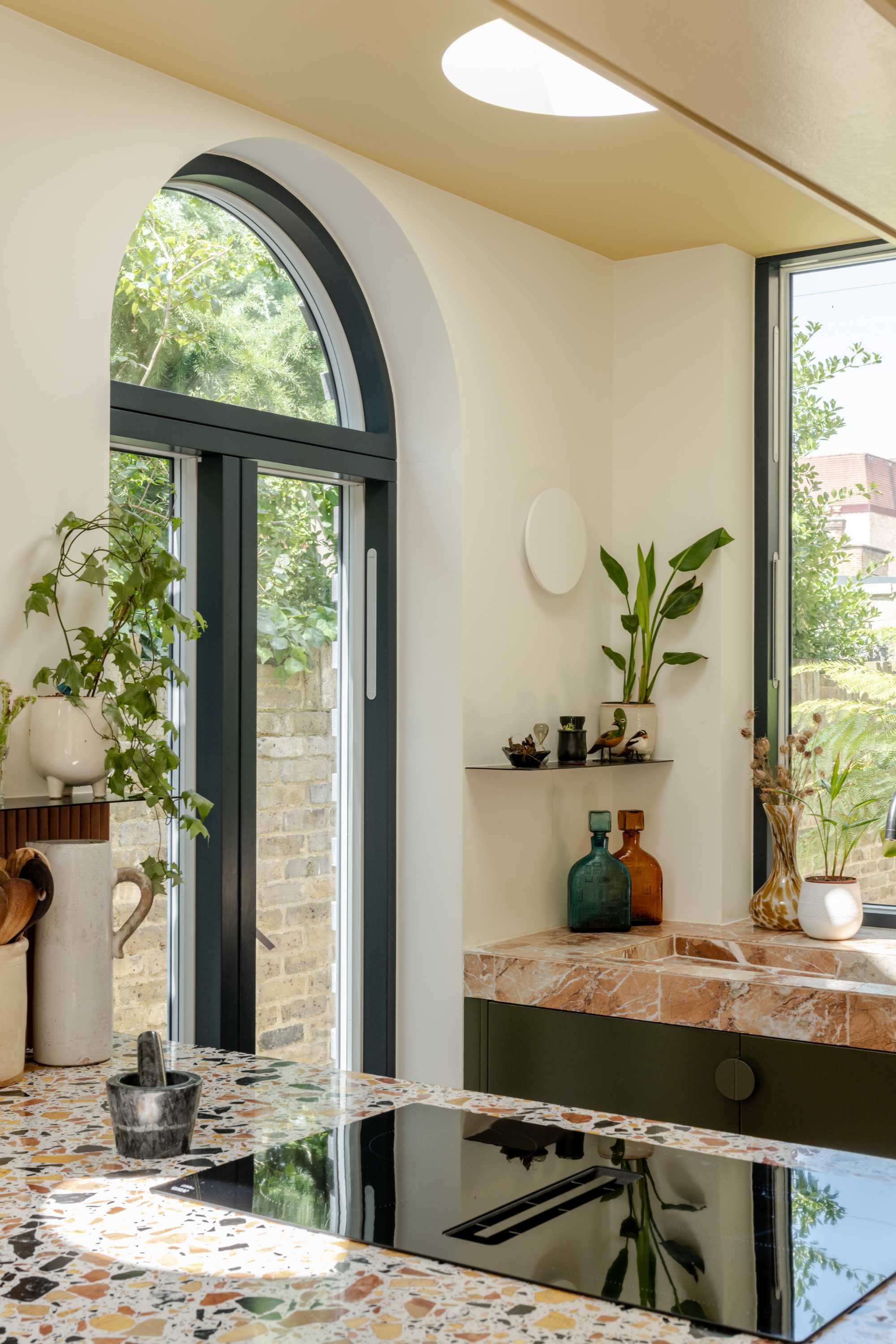 Modern kitchen extension with terrazzo flooring, black-framed arched window and glass doors creating open plan living space.